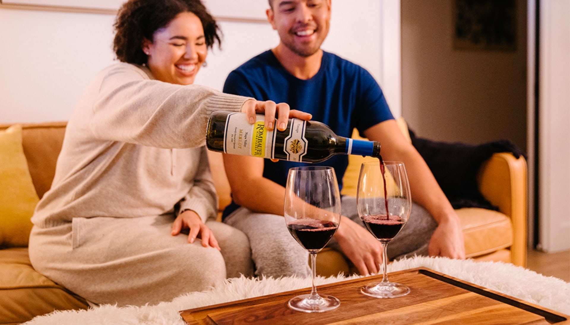 A couple sitting on their sofa pouring a glass of Rombauer red wine